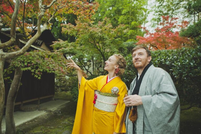 A woman in a yellow kimono points to a tree while standing next to a man in traditional Japanese clothing in a garden with colorful trees.