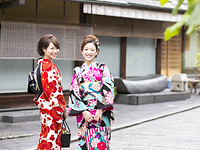 Two young women in colorful kimonos pose and smile on a traditional Japanese street.